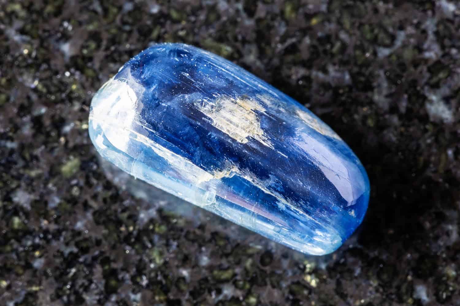 sample of tumbled blue kyanite gemstone on black granite background close up from Nepal