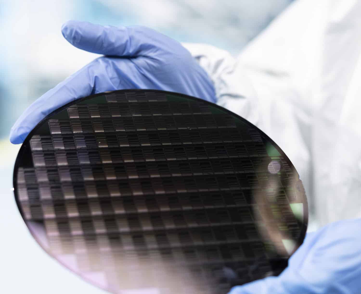 Close up of cleanroom engineer holding processed silicon wafer inside automated manufacturing facility. Technician inspecting delicate microelectronic hardware during quality control process