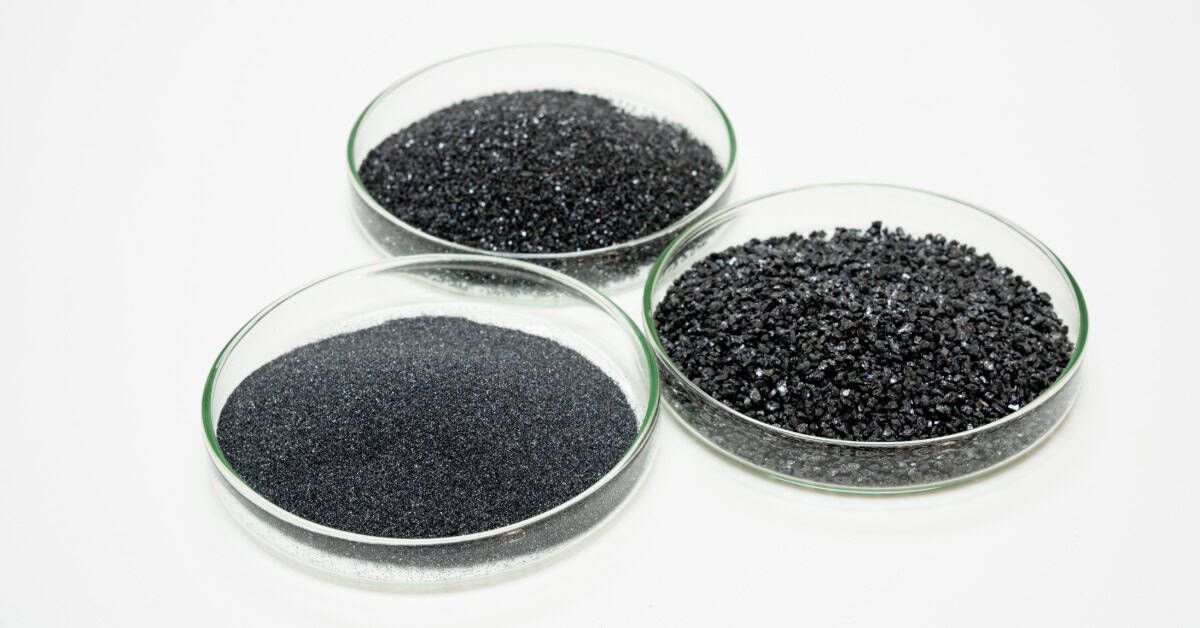 Three shallow glass dishes sit in a circle. One is filled with a black powder, and two are filled with tiny black pebbles.