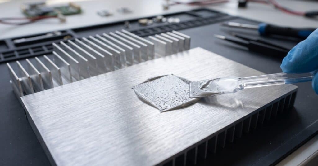 A close-up view shows a person wearing a latex glove spreading a thick paste on a metal surface with a plastic tool.