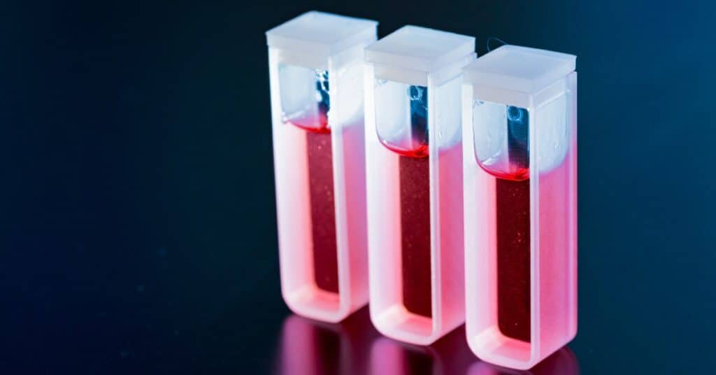 Three fused quartz cuvettes are filled with a pink liquid. They sit against a dark-gray background.