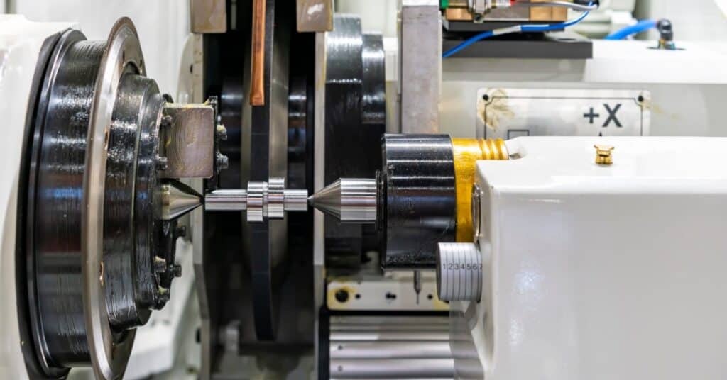 A white high-precision grinding machine is working to create a camshaft out of a piece of metal.
