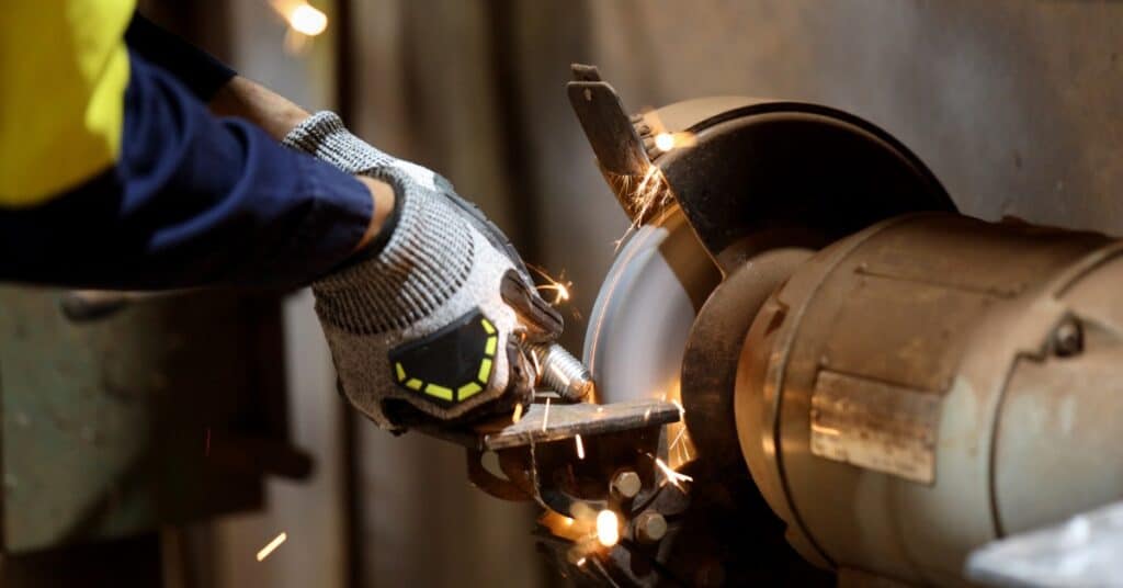 A close-up view shows a person wearing protective gloves and using a grinder to grind a piece of metal.